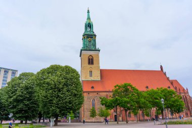 Berlin, Almanya - 1 Haziran 2025: Berlin 'deki tarihi St. Mary Kilisesi, belirgin bir kule ve canlı bir yeşilliğin yer aldığı, mimari ayrıntıları geliştiren bulutlu bir gökyüzüne karşı kurulmuştur..