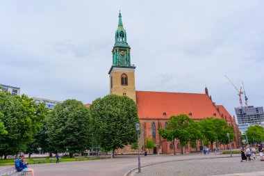 Berlin, Almanya - 1 Haziran 2025: Berlin 'deki tarihi St. Mary Kilisesi çarpıcı bir yeşil kuleye sahiptir ve bulutlu bir gökyüzü altında canlı ağaçların ve kentsel mimarinin bir zeminine karşıdır..