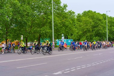 Berlin, Almanya - 1 Haziran 2025: Berlindeki verimli yeşil ağaçlarla çevrili geniş bir yolda sürüş yapan uzun bisiklet kuyruğu.