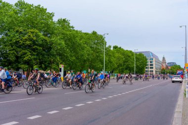 Berlin, Almanya - 1 Haziran 2025 Berlin 'de geniş bir cadde boyunca, yemyeşil ağaçlar ve modern mimariyle çevrili, dinamik bir şehir atmosferi yaratan sayısız bisikletçinin canlı sahnesi.