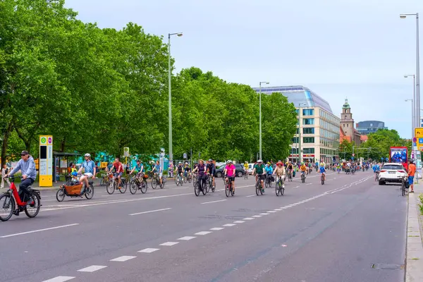 Berlin, Almanya - 1 Haziran 2025: Berlin 'de ağaçlık bir cadde boyunca birlikte giden bisikletçilerin canlı sokak manzarası, bulutlu gökyüzü altında kentsel ulaşım ve topluluk canlılığını gözler önüne seriyor.