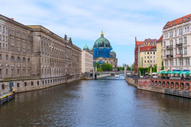 Berlin, Almanya - 1 Haziran 2025: İkonik Berlin Katedrali, Spree nehri boyunca uzanan tarihi yapılar tarafından çerçevelenmiş yeşil kubbesi açık mavi gökyüzü altında.