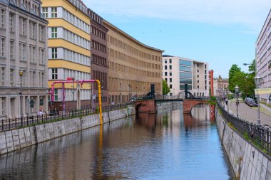 Berlin, Almanya - 1 Haziran 2025: Berlin 'deki şehir kanalı, berrak gökyüzü altında renkli binalar ve sakin su karışımının yer aldığı modern ve tarihi mimariyi yansıtıyor.