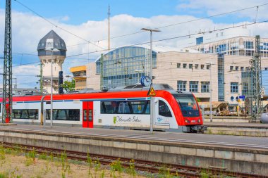 Darmstadt, Almanya - 16 Haziran 2025: Darmstadt istasyonuna canlı kırmızı ve beyaz renklerle gelen bölgesel tren, modern ulaşım ve tarihi mimari unsurların karışımını sergiliyor.