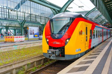 Darmstadt, Almanya - 16 Haziran 2025: Canlı kırmızı ve sarı bölgesel tren Darmstadt istasyonuna park edilmiş, modern mimari ve kentsel manzarayla çevrili, parlak gün ışığı altında.