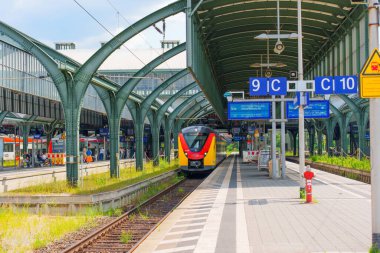 Darmstadt, Almanya - 16 Haziran 2025: Açık mavi gökyüzü altında çağdaş mimari ve canlı renklerin yer aldığı Darmstadt tren istasyonuna gelen tren.