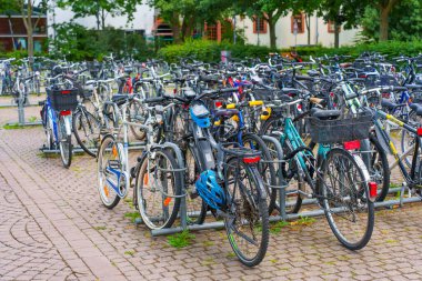 Darmstadt, Almanya - 16 Haziran 2025: Çevresi yeşil yeşilliklerle çevrili çeşitli bisikletlerle dolu bisiklet park alanı, canlı bir ortamda kentsel ulaşım seçenekleri sergiliyor.