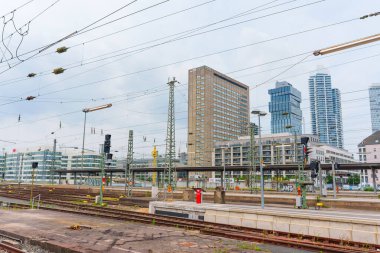 Frankfurt, Almanya - 10 Haziran 2025: Çağdaş binaların ve elektrik altyapısının bulunduğu Frankfurt siluetine giden tren rayları bulutlu bir gökyüzü altında.