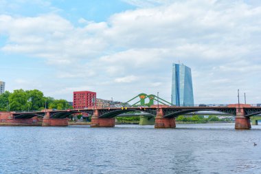 Frankfurt, Almanya - 10 Haziran 2025: Frankfurt 'un önemli bir köprü ve modern gökdelenleri parçalı bulutlu bir gökyüzü altında gösteren nehir manzarası.