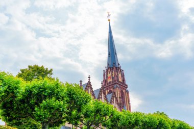 Frankfurt, Almanya - 10 Haziran 2025: Gotik tarzı kilise gökyüzünü noktalayan, yemyeşil ve dramatik bulutlarla çevrili, sakin ama görkemli bir atmosfer yaratıyor..