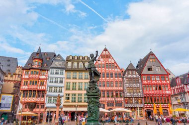Frankfurt, Almanya - 10 Haziran 2025: Rmerberg 'in canlı manzarası, Frankfurt' taki tarihi meydan, renkli ahşap çerçeveli evler ve bulutlu mavi gökyüzüne karşı bir heykel