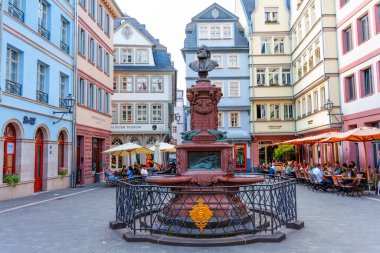 Frankfurt, Almanya - 10 Haziran 2025: Frankfurt 'ta canlı bir meydanda yer alan tarihi çeşme, tuhaf kafeler ve geleneksel mimari ile çevrili, yerel kültürün özünü yakalıyor.