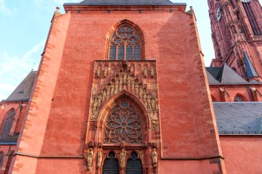Frankfurt, Almanya - 10 Haziran 2025: Frankfurt Katedrali 'nin kırmızı kumtaşı cephesinin ayrıntılı görüntüsü, süslü heykeller, vitray pencereler ve Gotik mimari unsurların yer aldığı.
