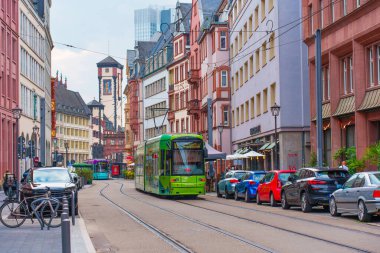 Frankfurt, Almanya - 10 Haziran 2025: Frankfurt 'ta yeşil bir tramvay, renkli arabalar ve bulutlu bir gökyüzü altında tarihi mimarinin yer aldığı canlı kentsel cadde.