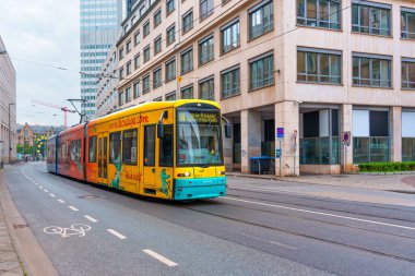Frankfurt, Almanya - 10 Haziran 2025: Çağdaş binalar ve kentsel unsurlarla çevrili Frankfurt 'ta şehir yolu boyunca seyahat eden canlı tramvay, kentsel bir ortamda modern ulaşımı gözler önüne seriyor.