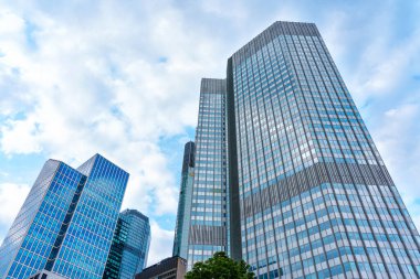 Frankfurt, Almanya - 10 Haziran 2025: Frankfurt 'ta mavi bulutlu gökyüzü altında çağdaş gökdelenlerin manzarası, parlak cam cepheler ve mimari tasarım sergileniyor.