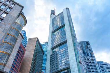 Frankfurt, Almanya - 10 Haziran 2025: Frankfurt, Almanya 'da dinamik ışıklandırma ve yansımalarla bulutlu bir gökdelenin altında yükselen modern gökdelenlerin yer aldığı dramatik kentsel ufuk çizgisi.