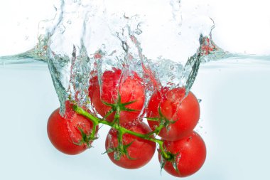 Temiz suya batırılmış taze kiraz domateslerinin dinamik sıçraması, parlak beyaz arka planda hareket ve tazeliği yakalar..