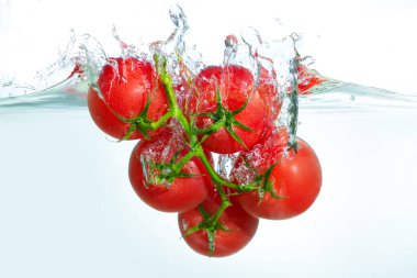 Yeşil bir sarmaşık üzerinde canlı kırmızı domatesler kristal berrak suya sıçrıyor etrafında kabarcıklar oluşuyor, parlak ışıkla aydınlatılıyor..