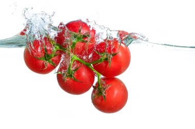 Canlı kırmızı kiraz domatesleri temiz suda dinamik sıçramalar yaratıyor. Temiz ve aydınlık bir ortamda tazelik ve canlılık sergiliyor..