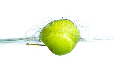 Temiz suya sıçrayan taze yeşil bir elmanın yakından görüntüsü parlak beyaz bir arka planda kabarcıklar ve dalgalanmalar yaratır..