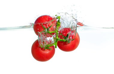 Canlı kırmızı domatesler kısmen berrak suya batmış, dinamik sıçramalar ve kabarcıklar yaratıyor, temiz bir ortamda tazelik ve canlılık vurgulanıyor..