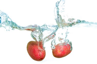 Temiz suda su sıçratan taze kırmızı patateslerin yakın plan görüntüsü pürüzsüz dokularını ve canlı renklerini vurguluyor..