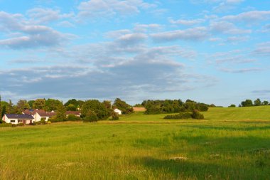 Berrak mavi gökyüzünün altında yemyeşil alanlar, dağınık bulutlar, Almanya 'nın Rossdorf kentindeki antika bir köyün yanında altın saat boyunca yuva yapmış..