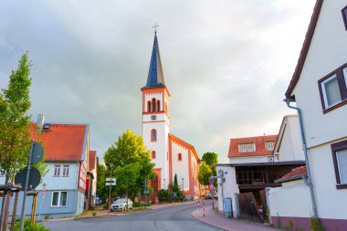 Rossdorf, Almanya - 23 Haziran 2025: Rossdorf, Almanya 'da tarihi bir kilise, geleneksel evler ve yumuşak doğal ışık altında sakin bir atmosfere sahip tuhaf bir köy manzarası.