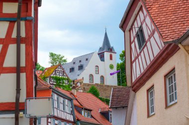 Zwingenberg, Almanya - 8 Haziran 2025: Zwingenberg 'in pitoresk köyünün özünü yakalamak için arka planda yükselen kilise kulesinin bulunduğu yemyeşil çerçeveli tuhaf yarı keresteli evler.