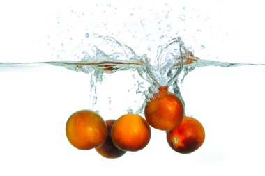 Temiz suya sıçrayan taze, olgun domateslerin yakın plan görüntüsü beyaz arka planda dinamik kabarcıklar ve dalgalanmalar yaratır..