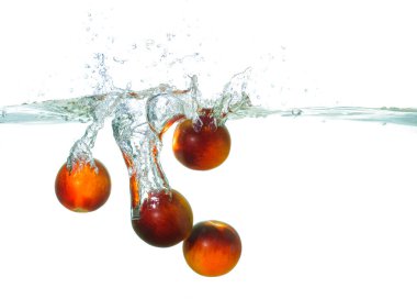 Temiz suya sıçrayan taze domateslerin yakın plan görüntüsü canlı kabarcıklar ve dalgalar yaratarak meyvenin canlandırıcı ve canlı doğasını gözler önüne seriyor..