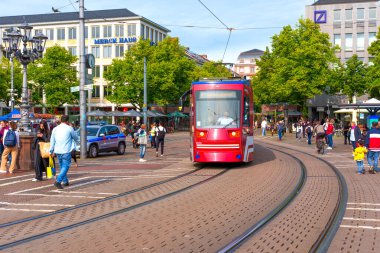 Darmstadt, Almanya - 5 Haziran 2025: Tramvay, Darmstadt 'ta yayalar, bisikletçiler ve yeşilliklerle dolu canlı bir meydanda güneşli bir günde kentsel yaşamı gözler önüne seriyor..