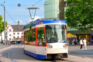 Darmstadt, Almanya - 5 Haziran 2025: Darmstadt, Almanya 'da bir istasyonda renkli tramvay, yayalar ve günışığı altında modern mimari ile çevrili.