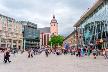 Köln, Almanya - 15 Haziran 2025: Köln 'de tarihi bir kilise, modern binalar ve bulutlu bir gökyüzü altında çeşitli faaliyetlerde bulunan kalabalıkların yer aldığı kalabalık.