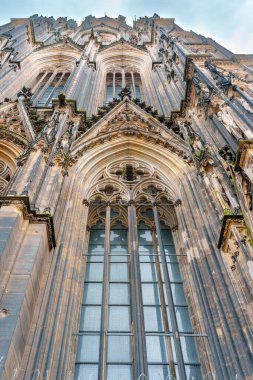 Köln, Almanya - 15 Haziran 2025: Köln Katedrali 'nin karmaşık taş işçiliğine ve boyalı camlarına yakından bakmak, Gotik mimari özellikleri ve atmosferik ışıklandırmayı vurgulamak.