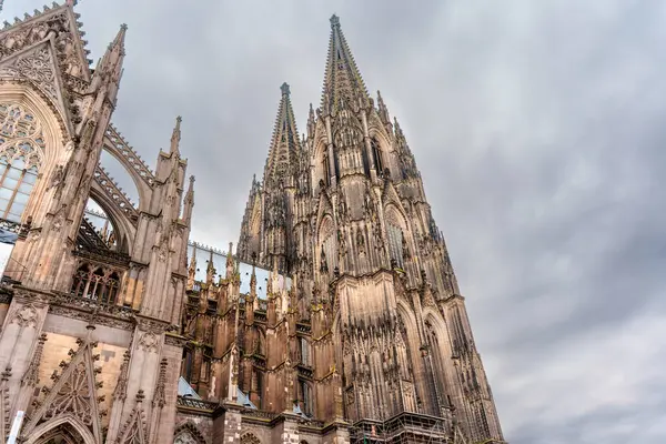 Köln, Almanya - 15 Haziran 2025: Köln Katedrali 'nin karmaşık Gotik detayları, yüksek kuleler ve kasvetli, bulutlu gökyüzü altında süslü heykeller.