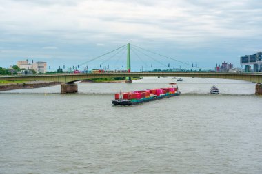 Köln, Almanya - 15 Haziran 2025: Kargo gemisi Köln, Almanya 'daki Hohenzollern Köprüsü' nün altındaki huzurlu Ren Nehri üzerinde renkli konteynırlar taşıyor.