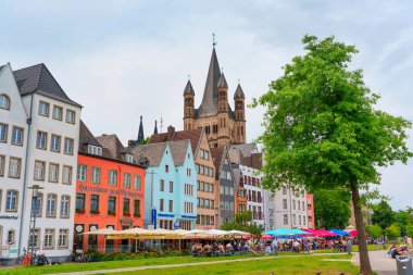 Köln, Almanya - 15 Haziran 2025: Renkli nehir kıyısındaki binalar ve tarihi bir katedral, canlı şehir yaşamını ve mimarisini yansıtan, Köln 'deki Ren nehri boyunca pitoresk bir manzara yarattı..