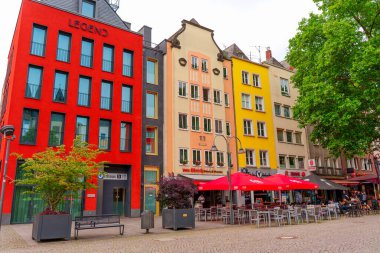 Köln, Almanya - 15 Haziran 2025: Cologne 'da canlı bir sokak sahnesinde, açık hava oturma alanlarıyla kırmızı, sarı ve pastel renklerin karışımını gösteren canlı binalar.