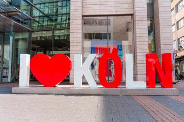 Köln, Almanya - 15 Haziran 2025: Vibrant I Love Koeln tabelası modern mimarinin önünde, şehrin gündüz saatlerinde kültürel kimliğini ve çekiciliğini yansıtıyor..