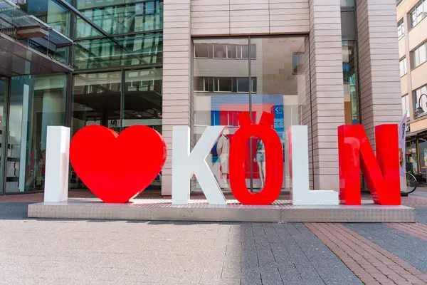 Köln, Almanya - 15 Haziran 2025: Vibrant I Love Koeln tabelası modern mimarinin önünde, şehrin gündüz saatlerinde kültürel kimliğini ve çekiciliğini yansıtıyor..