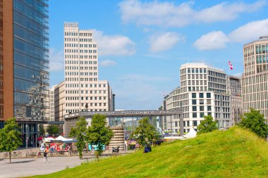 Berlin, Almanya - 16 Ağustos 2025: Modern mimari, yeşil çimenlik alanlar ve Berlin 'deki kentsel yaşamı yansıtan açık mavi bir gökyüzü içeren hareketli Potsdamer Platz manzarası.
