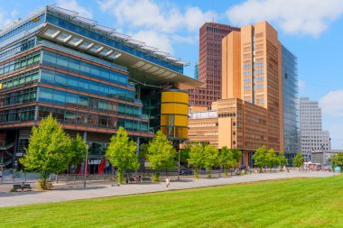Berlin, Almanya - 16 Ağustos 2025: Berlinde Potsdamer Platz, Berlin 'deki Daimler City kompleksinde canlı kentsel binalar, yemyeşil ve açık mavi gökyüzü.