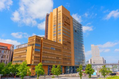 Berlin, Almanya - 16 Ağustos 2025: Kollhoff Kulesi ve Atrium Kulesi 'nin mimari detayları Potsdamer Platz' da açık mavi gökyüzüne karşı, canlı kent tasarımı ve yeşillik sergilenmektedir..