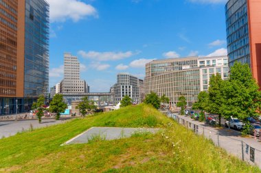 Berlin, Almanya - 16 Ağustos 2025: Berlin 'in Potsdamer Platz bölgesinde açık mavi gökyüzü altında modern binalar ve yeşil alanlar içeren şehir manzarası.