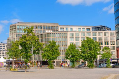 Berlin, Almanya - 16 Ağustos 2025: Canlı bir Berlin meydanında yemyeşil ve kentsel yaşamla çevrili geniş cam cepheli çağdaş binalar.