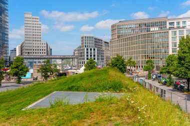 Berlin, Almanya - 16 Ağustos 2025: Bahnhof Potsdamer Platz, Berlin 'deki modern mimari yapılar ve verimli yeşillik, berrak mavi gökyüzü altında canlı bir şehir manzarası sergiliyor..