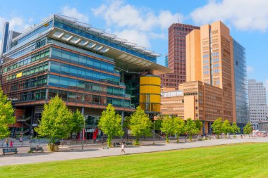 Berlin, Almanya - 16 Ağustos 2025: Kollhoff Kulesi ve Atrium Kulesi 'nin Potsdamer Platz, Berlin' deki yeşilliklerle çevrili mimari görünümü, modern tasarım ve kentsel manzara.