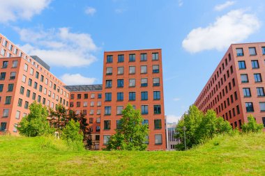 Berlin, Almanya - 16 Ağustos 2025: Park Kolonnaden, Berlin 'deki çağdaş apartmanlar, büyük pencereler, yeşil peyzaj ve şehir manzarasını vurgulayan açık mavi bir gökyüzü.